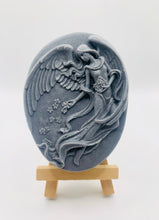 Load image into Gallery viewer, Handmade vegan Guardian Angel soap bar in a peach-toned French clay, featuring a detailed angel relief with flowing wings and flowers. Displayed on a small wooden easel. Natural, cruelty-free UK soap ideal for spiritual gifts, zero waste skincare, and sustainable bathroom décor. British-made artisan soap perfect for eco-conscious shoppers
