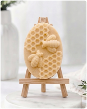 Load image into Gallery viewer, handmade vegan soap featuring an oval relief sculpture of two honey bees crawling on a honeycomb pattern, displayed on a small wooden easel in a bright farmhouse decor setting.