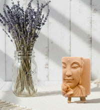 Load image into Gallery viewer, handmade vegan soap featuring a detailed 3D relief of a serene Buddha face with a lotus flower, displayed on a wooden easel against a whimsical farmhouse decor background.