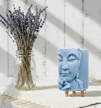 Load image into Gallery viewer, handmade vegan soap featuring a detailed 3D relief of a serene Buddha face with a lotus flower, displayed on a wooden easel against a whimsical farmhouse decor background.