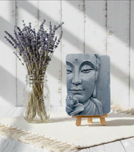 Load image into Gallery viewer, handmade vegan soap featuring a detailed 3D relief of a serene Buddha face with a lotus flower, displayed on a wooden easel against a whimsical farmhouse decor background.