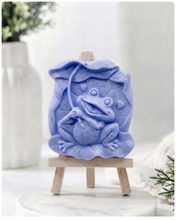 Load image into Gallery viewer, A rectangular handmade vegan soap featuring a high-relief carving of a cheerful, smiling frog sitting on a large lilypad and holding the stem of a leaf over its head like an umbrella.