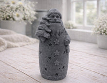 Load image into Gallery viewer, handmade vegan soap sculpted into a tall figure of Father Christmas wearing star-patterned robes, holding a small Christmas tree in one arm and a lantern in the other, set in a bright farmhouse window.