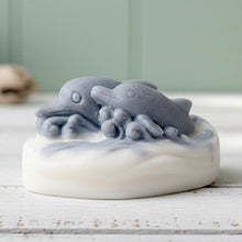 Load image into Gallery viewer, A handmade vegan soap featuring two grey dolphins jumping through white frothy waves; the base is white, and the dolphins are highly detailed, displayed on a light wooden surface against a soft farmhouse background.