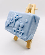 Load image into Gallery viewer, Handmade vegan soaps featuring a boy and girl sat on a bench with the wording Love Is... , in beautiful eco friendly packaging. crafted with natural French clays, activated charcoal and essential oils. a eco-friendly, zero waste gift that’s cruelty-free, skin-nourishing, the perfect gift for Valentines day or anniversary gift. small business UK