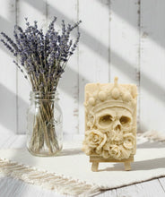 Load image into Gallery viewer, A handmade vegan soap featuring a highly detailed 3D relief of a skull wearing a jewelled crown and surrounded by roses, displayed on a wooden easel against a whimsical background.