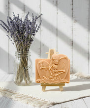 Load image into Gallery viewer, A spooky handmade vegan soap featuring a 3D relief of a skeleton relaxing against "RIP" tombstones, displayed on a wooden easel against a whimsical farmhouse decor background.