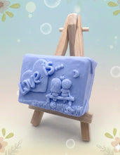 Load image into Gallery viewer, Handmade vegan soaps featuring a boy and girl sat on a bench with the wording Love Is... , in beautiful eco friendly packaging. crafted with natural French clays, activated charcoal and essential oils. a eco-friendly, zero waste gift that’s cruelty-free, skin-nourishing, the perfect gift for Valentines day or anniversary gift. small business UK