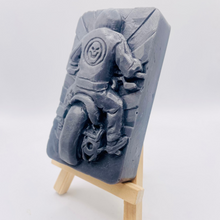 Load image into Gallery viewer, detailed handmade vegan soap gift featuring a motorcycle rider with a skull emblem on their jacket, displayed on a wooden easel against a whimsical farmhouse decor background