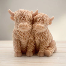 Load image into Gallery viewer, Handmade soap featuring two Highland cows with textured, shaggy fur sitting side by side on a light wooden surface with a softly indoor background.