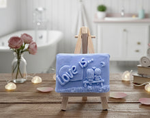 Load image into Gallery viewer, Handmade vegan soaps featuring a boy and girl sat on a bench with the wording Love Is... , in beautiful eco friendly packaging.