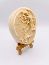 Load image into Gallery viewer, Handmade vegan Guardian Angel soap bar in a peach-toned French clay, featuring a detailed angel relief with flowing wings and flowers. Displayed on a small wooden easel. Natural, cruelty-free UK soap ideal for spiritual gifts, zero waste skincare, and sustainable bathroom décor. British-made artisan soap perfect for eco-conscious shoppers
