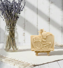 Load image into Gallery viewer, A spooky handmade vegan soap featuring a 3D relief of a skeleton relaxing against "RIP" tombstones, displayed on a wooden easel against a whimsical farmhouse decor background.