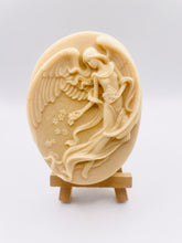 Load image into Gallery viewer, Handmade vegan Guardian Angel soap bar in a peach-toned French clay, featuring a detailed angel relief with flowing wings and flowers. Displayed on a small wooden easel. Natural, cruelty-free UK soap ideal for spiritual gifts, zero waste skincare, and sustainable bathroom décor. British-made artisan soap perfect for eco-conscious shoppers