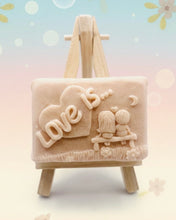 Load image into Gallery viewer, Handmade vegan soaps featuring a boy and girl sat on a bench with the wording Love Is... , in beautiful eco friendly packaging. crafted with natural French clays, activated charcoal and essential oils. a eco-friendly, zero waste gift that’s cruelty-free, skin-nourishing, the perfect gift for Valentines day or anniversary gift. small business UK