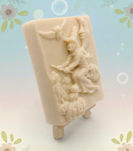 Load image into Gallery viewer, A beautiful handmade vegan soap featuring a detailed image of a witch flying on a broomstick past a crescent moon and owls, displayed on a wooden easel against a whimsical farmhouse decor background.