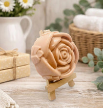 Load image into Gallery viewer, A handmade vegan soap, intricately sculpted in the shape of a large, blooming rose flower with layered petals, displayed on a small wooden easel against a bright win