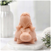 Load image into Gallery viewer, A handmade vegan soap in a warm terracotta-peach tone, sculpted as a whimsical gnome (gonk) with a long, flowing beard sitting on the back of a large, smiling ladybird with visible spots, displayed on a light wooden surface.