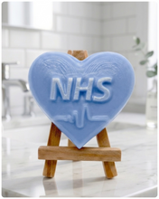 Load image into Gallery viewer, handmade vegan soap in a heart shape featuring an "NHS" relief and a heartbeat pulse line, displayed on a small wooden easel