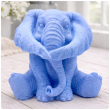 Load image into Gallery viewer, A crisp product photograph of a detailed, grey artisan bar of soap intricately moulded into the shape of a sitting baby elephant. The elephant is depicted holding its trunk with its front legs crossed in a "hear no evil" or hugging pose, showcasing realistic skin textures, expressive eyes, and large ears.