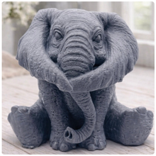 Load image into Gallery viewer, A crisp product photograph of a detailed, grey artisan bar of soap intricately moulded into the shape of a sitting baby elephant. The elephant is depicted holding its trunk with its front legs crossed in a "hear no evil" or hugging pose, showcasing realistic skin textures, expressive eyes, and large ears.
