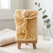Load image into Gallery viewer, A rectangular handmade vegan soap featuring a detailed relief of a winged fairy reaching towards a butterfly in a meadow of tall grass and flowers, displayed on a wooden easel