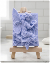 Load image into Gallery viewer, A rectangular handmade vegan soap, featuring a high-relief carving of a seated fairy with large, detailed wings holding a single blossom, displayed on a miniature wooden easel.