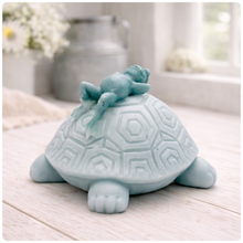 Load image into Gallery viewer, A handmade vegan soap in a soft mint green tone, sculpted into a large friendly turtle with a geometric shell pattern and a small, cute frog sleeping peacefully on its back.