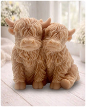 Load image into Gallery viewer, Handmade soap featuring two Highland cows with textured, shaggy fur sitting side by side on a light wooden surface with a softly indoor background.
