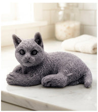 Load image into Gallery viewer, A highly detailed handmade vegan soap sculpted in the shape of a sitting cat with its tail curled around its paws, featuring realistic fur texture and a sweet facial expression, displayed on a light wooden surface.