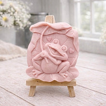 Load image into Gallery viewer, A rectangular handmade vegan soap featuring a high-relief carving of a cheerful, smiling frog sitting on a large lilypad and holding the stem of a leaf over its head like an umbrella.