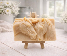 Load image into Gallery viewer, A rectangular handmade vegan soap featuring a detailed relief of two horse heads leaning affectionately towards each other, finished in soft natural tones and displayed on a miniature wooden easel.