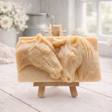 Load image into Gallery viewer, A rectangular handmade vegan soap featuring a detailed relief of two horse heads leaning affectionately towards each other, finished in soft natural tones and displayed on a miniature wooden easel.