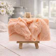 Load image into Gallery viewer, A rectangular handmade vegan soap featuring a detailed relief of two horse heads leaning affectionately towards each other, finished in soft natural tones and displayed on a miniature wooden easel.