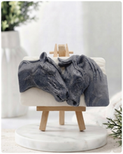 Load image into Gallery viewer, A rectangular handmade vegan soap featuring a detailed 3D relief of two horse heads leaning affectionately towards each other, finished in a slate-grey tone against a white soap base and displayed on a miniature wooden easel.