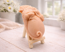Load image into Gallery viewer, A 3D handmade vegan soap in a charcoal-grey tone, sculpted as a large prehistoric egg with a small dinosaur or dragon clinging to the top, featuring detailed scales and a curled tail, displayed on a miniature wooden easel.