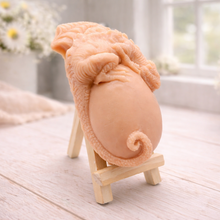 Load image into Gallery viewer, A 3D handmade vegan soap in a charcoal-grey tone, sculpted as a large prehistoric egg with a small dinosaur or dragon clinging to the top, featuring detailed scales and a curled tail, displayed on a miniature wooden easel.