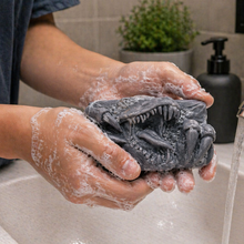 Load image into Gallery viewer, Person washing with dinosaur charcoal soap bar with foam in a sink.