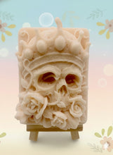 Load image into Gallery viewer, A handmade vegan soap featuring a highly detailed 3D relief of a skull wearing a jewelled crown and surrounded by roses, displayed on a wooden easel against a whimsical background.