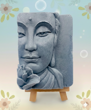 Load image into Gallery viewer, handmade vegan soap featuring a detailed 3D relief of a serene Buddha face with a lotus flower, displayed on a wooden easel against a whimsical farmhouse decor background.