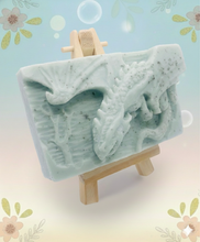 Load image into Gallery viewer, Dragon gift. Dinosaur gift. Our Flying Dragon soap features a striking dragon with its majestic wings spread wide, symbolising freedom and power. This artisan bar is vegan, cruelty-free, and designed with care for both your skin and the planet. Available in your choice of colour and essential oil. Each soap comes beautifully wrapped in eco friendly packaging. zero waste gift. kodern gift ideas. handmade home style. eco conscious home. eco friendly gifts. go green home.