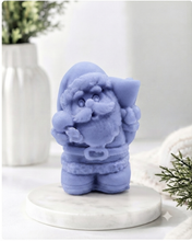 Load image into Gallery viewer, A highly detailed 3D handmade vegan soap featuring a Father Christmas carrying a large sack of gifts over his shoulder and holding a bell, featuring an intricate curly beard and fur-trimmed suit, set against a festive holiday background.