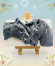 Load image into Gallery viewer, A grey and white handmade vegan soap featuring a highly detailed relief of two horses nuzzling heads, displayed on a wooden easel against a whimsical farmhouse decor background.