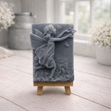 Load image into Gallery viewer, A rectangular handmade vegan soap featuring a detailed relief of a winged fairy reaching towards a butterfly in a meadow of tall grass and flowers, displayed on a miniature wooden easel