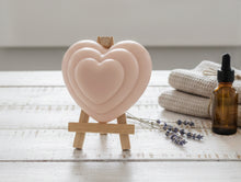 Load image into Gallery viewer, Heart-shaped vegan soap on a wooden stand with a bottle and lavender on a light surface