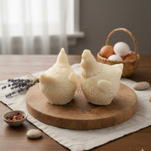 Load image into Gallery viewer, Two chicken-shaped vegan soaps on a wooden board with a basket of eggs in the background.