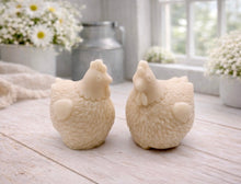 Load image into Gallery viewer, Two handmade vegan soaps in the shape of plump, realistic chicken sculptures with detailed feather textures, displayed on a rustic white wooden surface in a bright farmhouse decor setting.