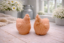 Load image into Gallery viewer, Two handmade vegan soaps in the shape of plump, realistic chicken sculptures with detailed feather textures, displayed on a rustic white wooden surface in a bright farmhouse decor setting.