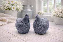 Load image into Gallery viewer, Two handmade vegan soaps in the shape of plump, realistic chicken sculptures with detailed feather textures, displayed on a rustic white wooden surface in a bright farmhouse decor setting.
