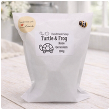 Load image into Gallery viewer, White bag of handmade soap labeled 'Turtle & Frog' on a light wooden surface with flowers in the background.